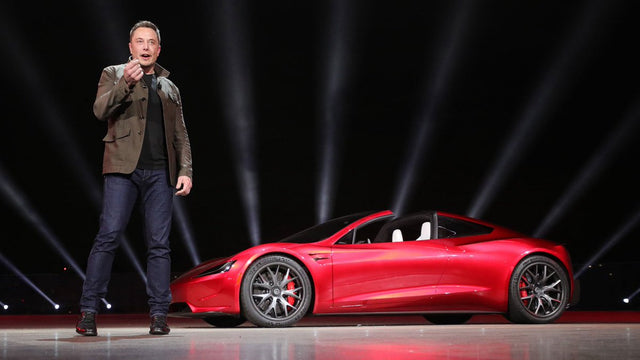 Elon Musk standing beside a red Tesla Roadster prototype at a reveal event; historical event photo, not a current trim-price chart